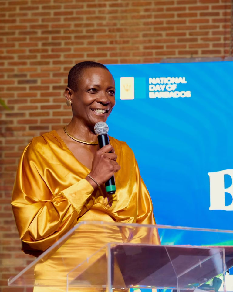 Embaixadora de Barbados sorri ao microfone, em vestido dourado, discursando no púlpito