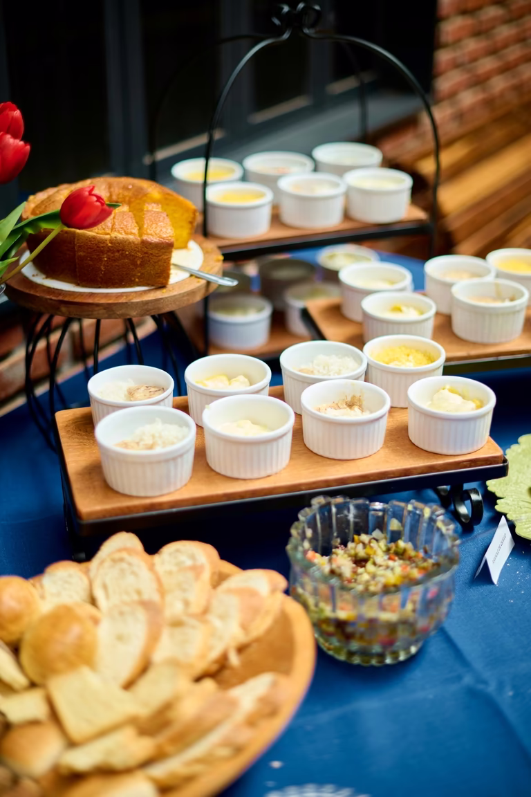 Mesa de buffet com pães, patês em ramequins e bolo sobre toalha azul