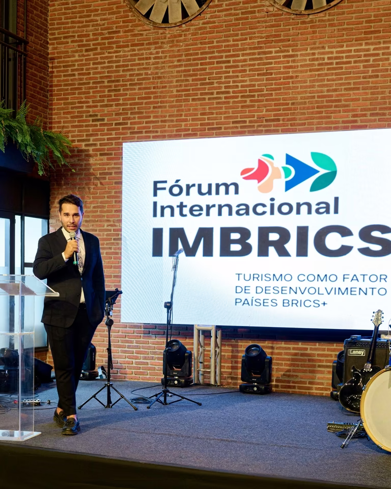 Palestrante no palco do Fórum Internacional IMBRICS+ diante do telão com a marca do evento