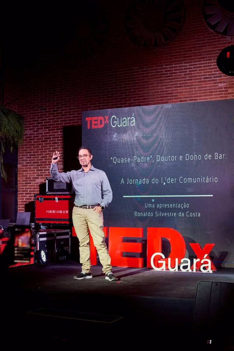 Palestrante brinda no palco com o telão do TEDx Guará exibindo o tema da talk
