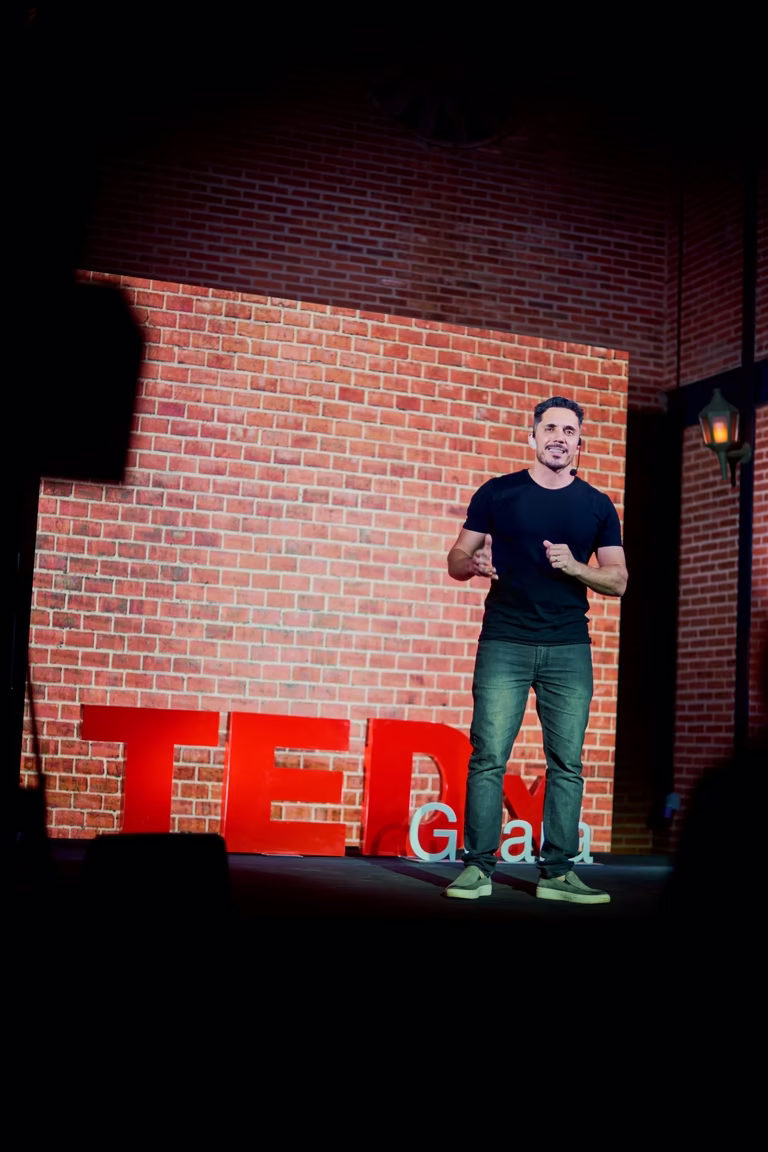 Palestrante no palco do TEDx diante do muro de tijolos com as letras TEDx