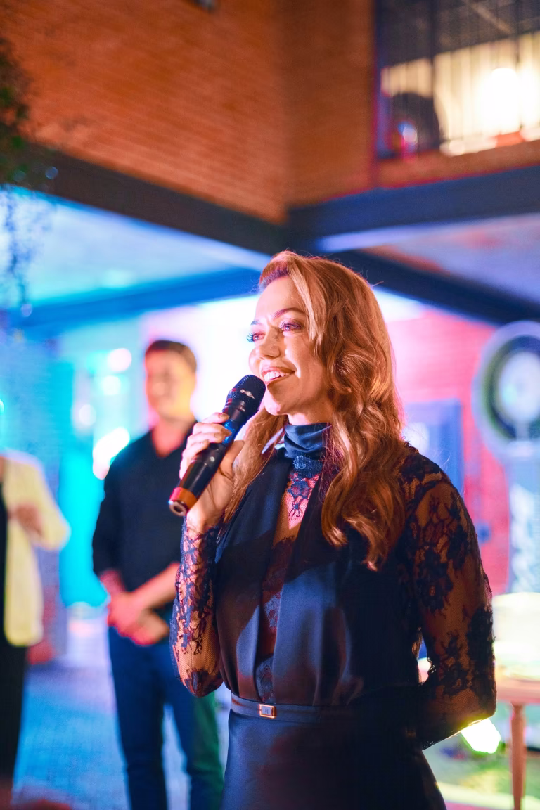 Anfitriã sorridente fala ao microfone durante o evento noturno